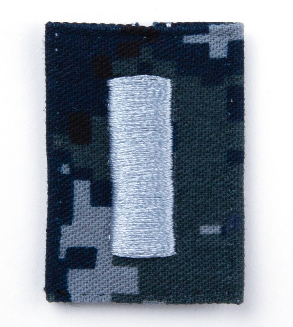 US NAVY Working Uniform Type 1 Cap Device - O-2 Lieutenant Junior Grade. Silver embroidery on Blueberry Camo.  Official U.S. Navy patch worn on the NAVY NWU Type I 8-Point Cover. Digital Blue Camouflage (retired in October 2019).  - USN Certified - NWU Type 1 Blue Digital Camouflage (Blueberries) - Individually sold - Fabric: 50% Nylon / 50% Cotton Twill - Made in the USA - Condition: Good, pre-owned/gently used unless marked as NEW.